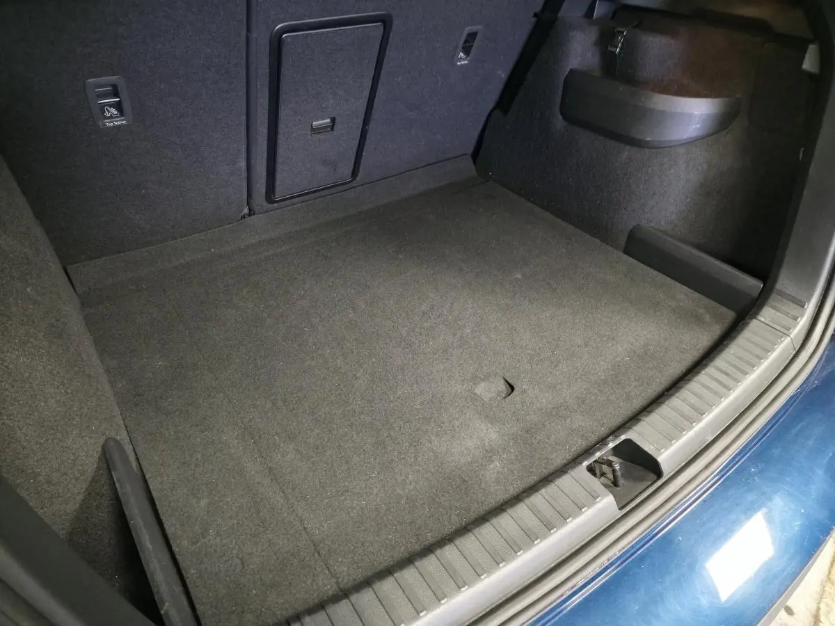Vue plongeante sur le coffre spacieux et propre du Skoda Karoq bleu 2024, avec moquette noire et trappe centrale.