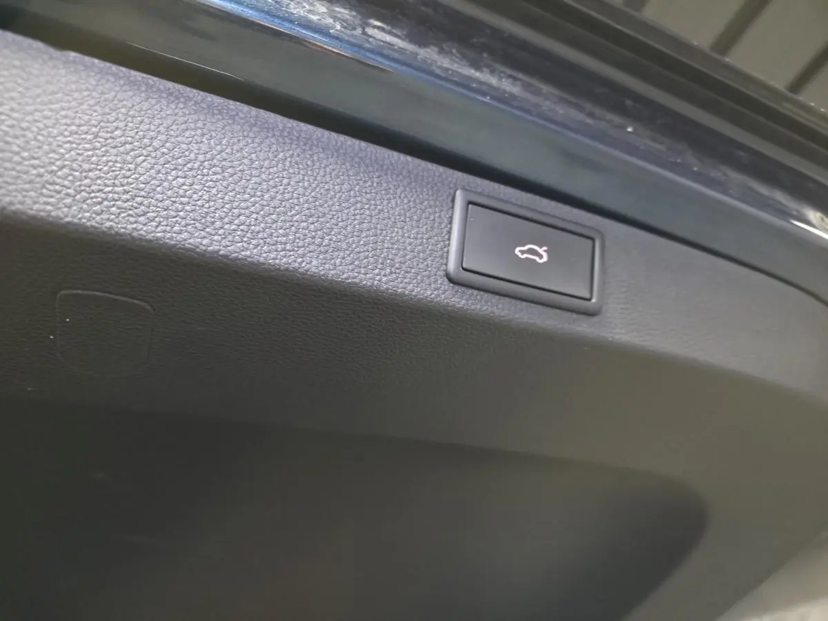 Gros plan sur le bouton d'ouverture électrique du hayon du Skoda Karoq bleu, intérieur du coffre visible.