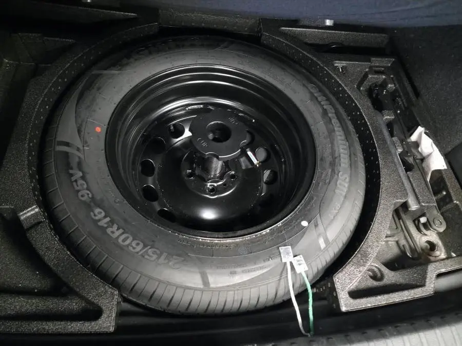 Gros plan sur la roue de secours temporaire noire dans le coffre du Skoda Karoq bleu 2024.