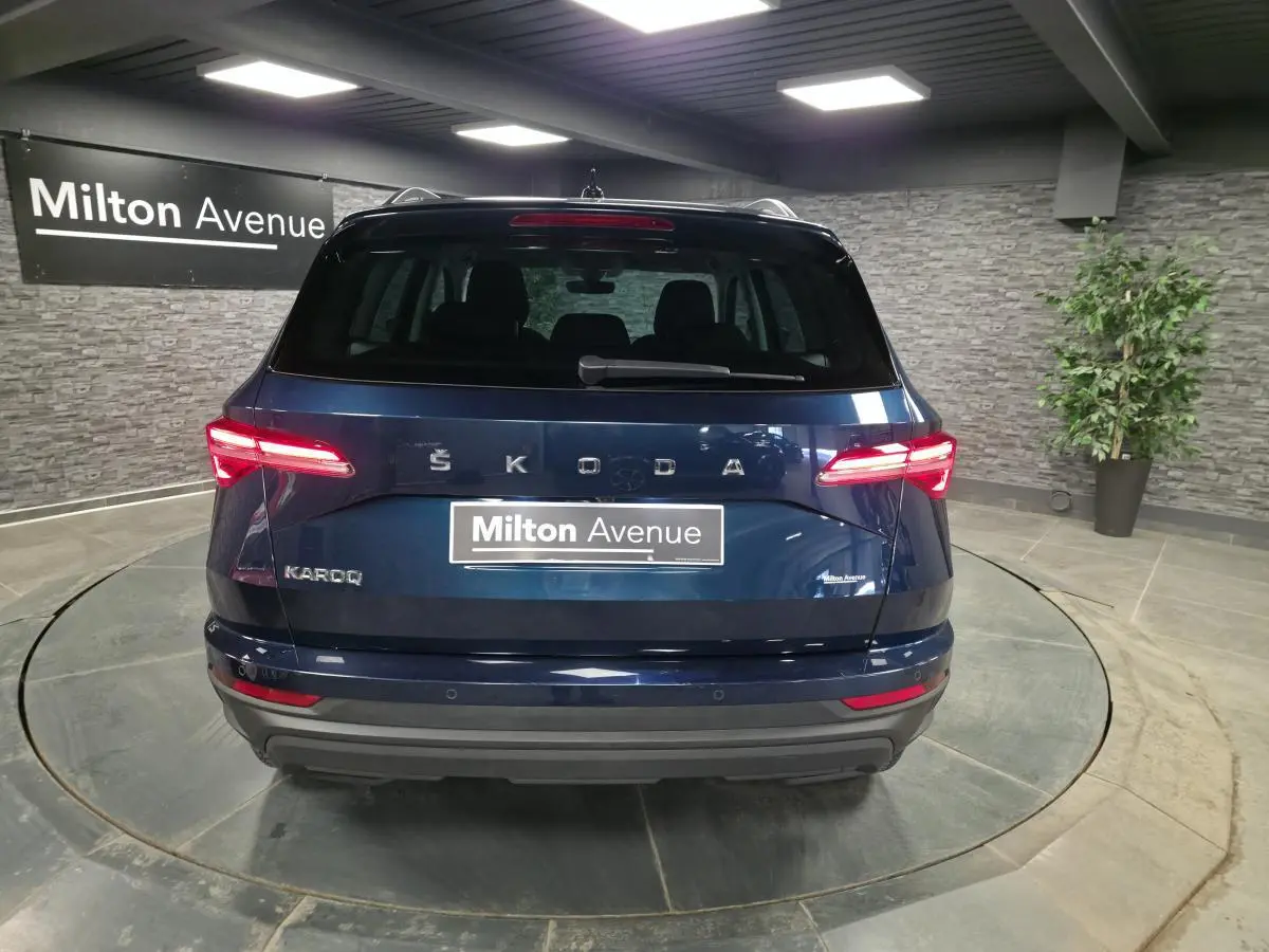 Vue arrière d'un Skoda Karoq bleu métallisé 2024 avec feux LED et logo SKODA visible sur fond intérieur showroom.