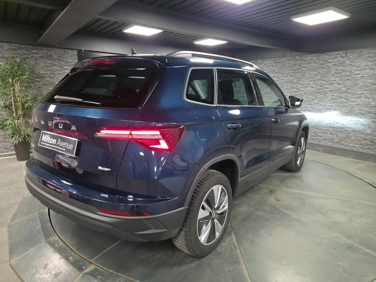 Vue 3/4 arrière droite d'un Skoda Karoq bleu métallisé 2024 avec feux arrière LED et jantes alliage 17 pouces.