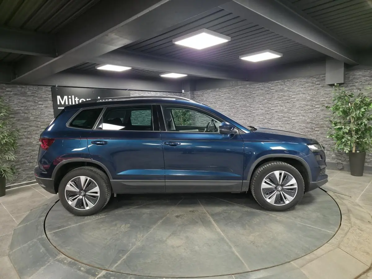 Vue latérale droite d'un Skoda Karoq bleu métallisé 2024 dans un showroom avec jantes alliage 17 pouces.