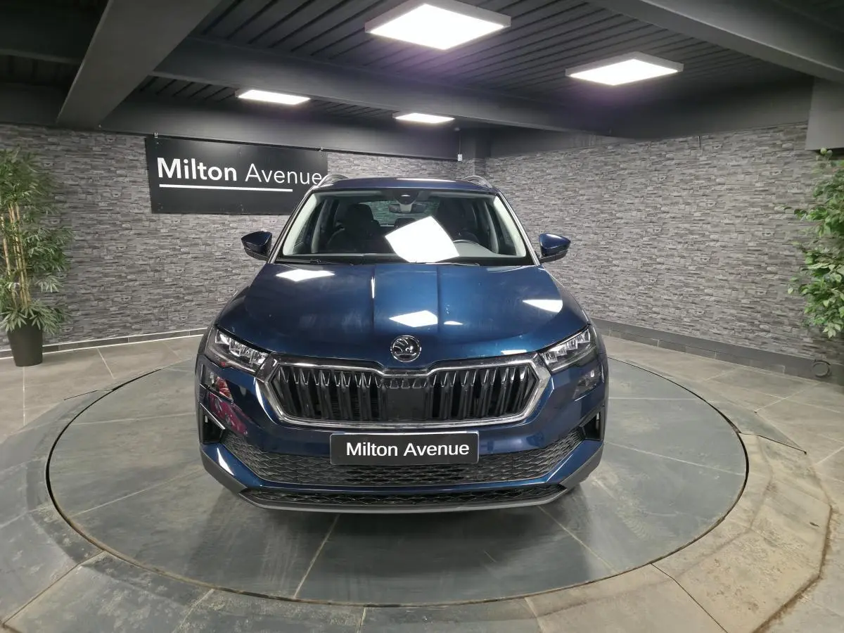 Vue frontale d'un Skoda Karoq bleu métallisé 2024 dans un showroom avec calandre noire et logo central.