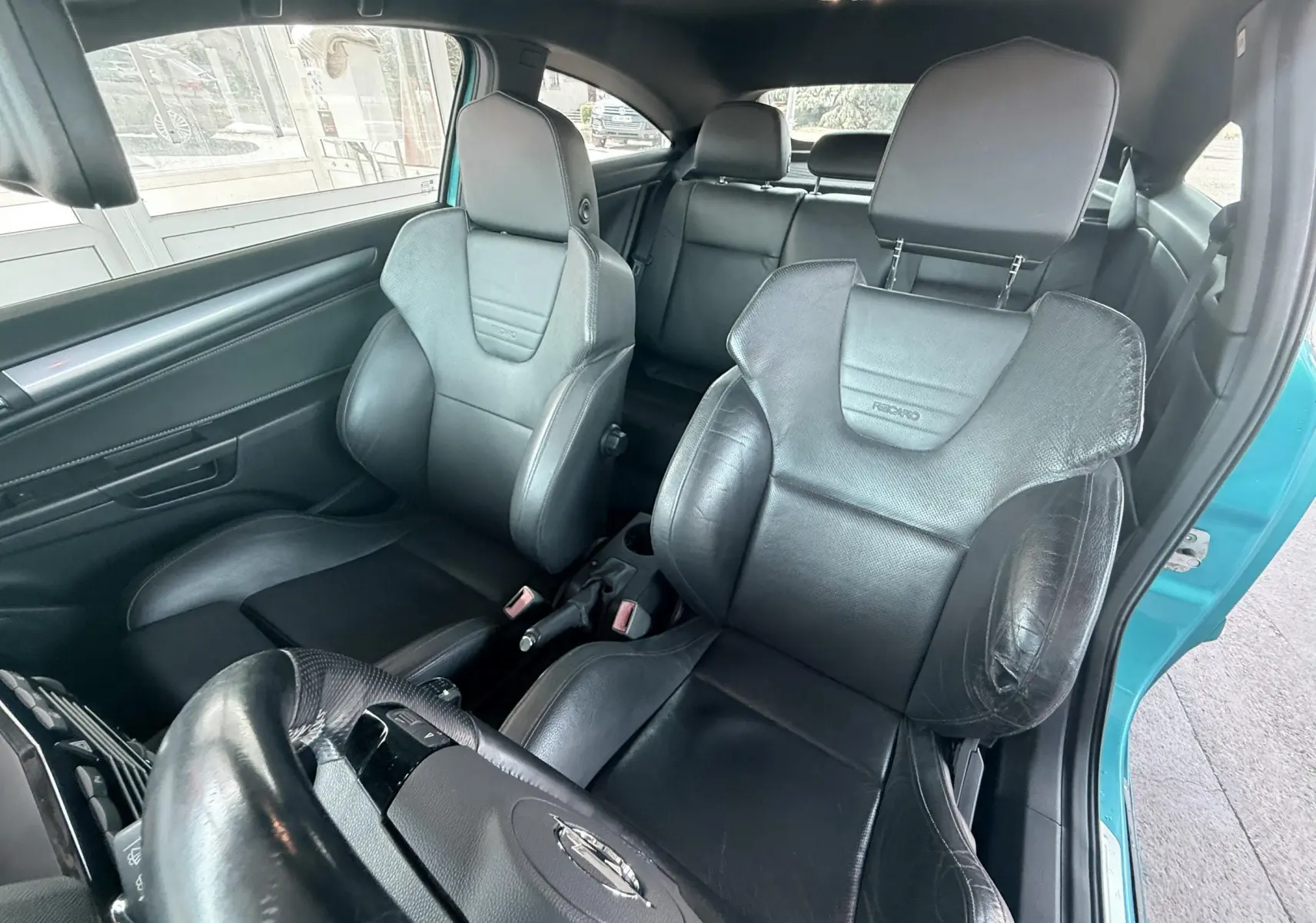 Vue intérieure avant droite sur les sièges baquets noirs Recaro d’une Opel Astra OPC bleu visible à l’ouverture de la porte.
