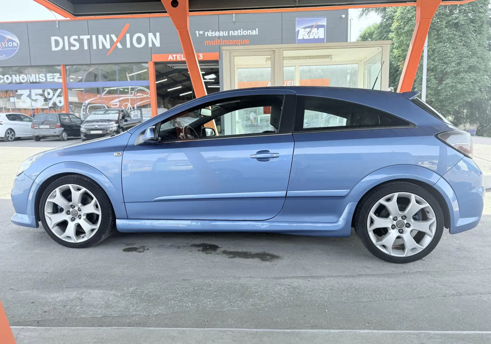 Profil côté gauche d'une Opel Astra OPC 2008 bleu avec jantes sport et toit noir sous un abri.