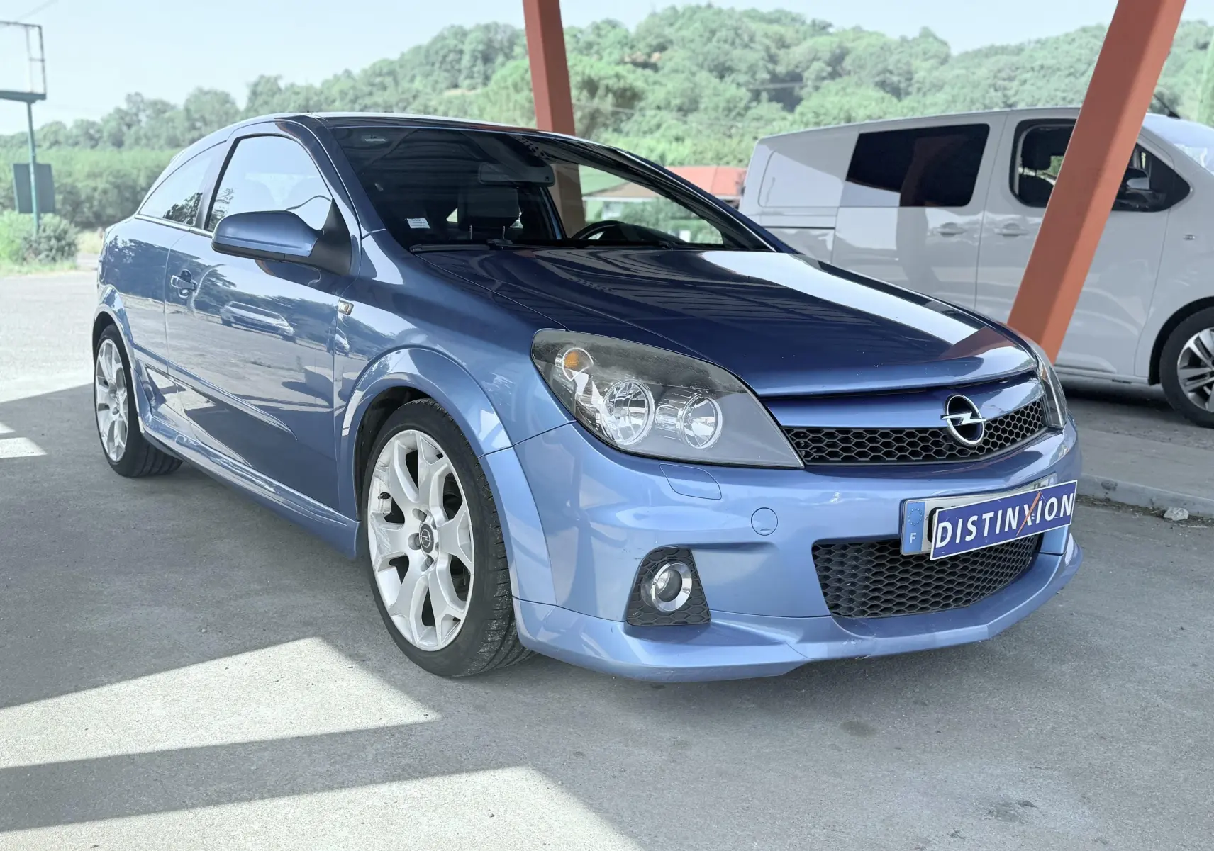 Opel Astra OPC bleu vue 3/4 avant droit sous abri avec jantes alliage et calandre noire.