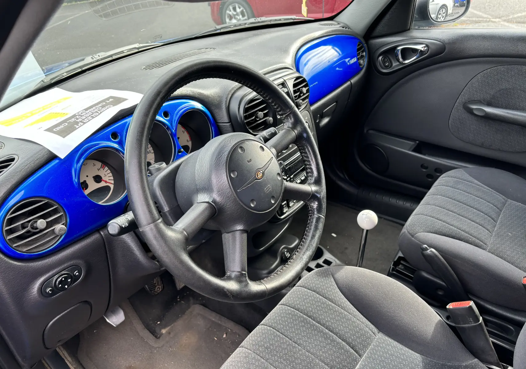 Vue intérieure côté conducteur du Chrysler PT Cruiser 2004, tableau de bord bleu vif et levier de vitesse manuel blanc.