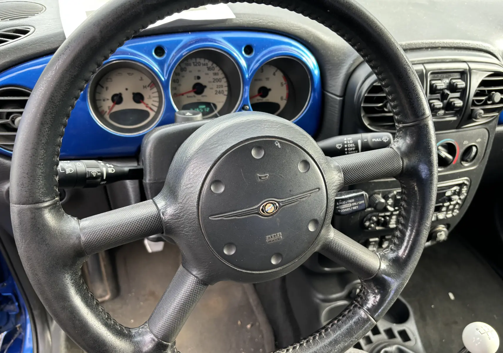 Vue rapprochée du volant noir et du tableau de bord bleu du Chrysler PT Cruiser 2004 diesel avec boîte manuelle.