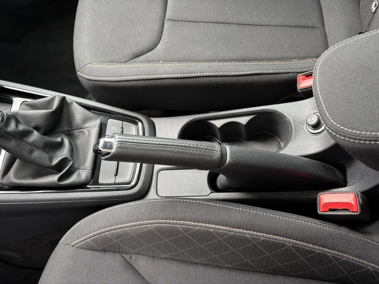 Vue plongeante sur la console centrale du Skoda Kamiq 2024, montrant frein à main manuel et sièges tissu noirs.