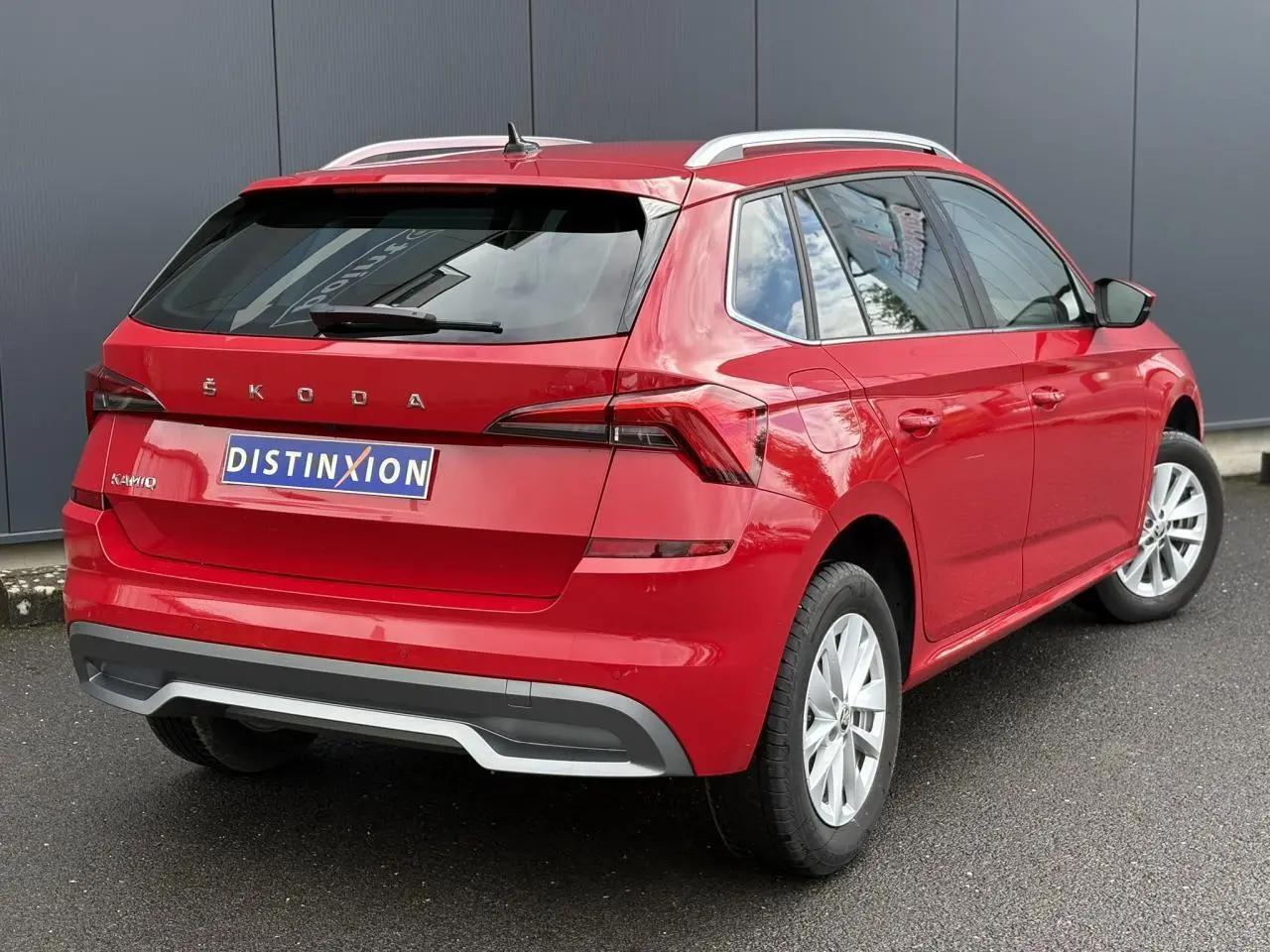 Vue 3/4 arrière droite d'un Skoda Kamiq 2024 rouge Velvet avec jantes alliage et barres de toit alu.