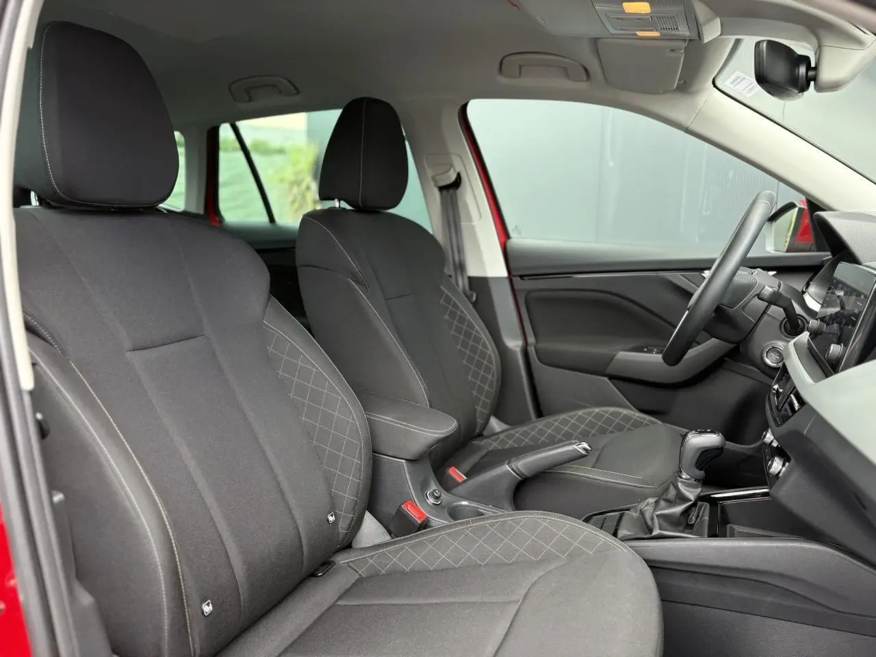Vue intérieure côté conducteur du Skoda Kamiq rouge Velvet 2024, sièges noirs avec coutures contrastées et volant multifonctions.