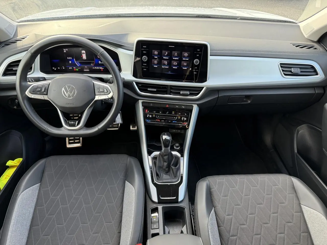 Intérieur du Volkswagen T-Roc 2025 vu de face, avec tableau de bord digital et sièges tissu noir et gris.
