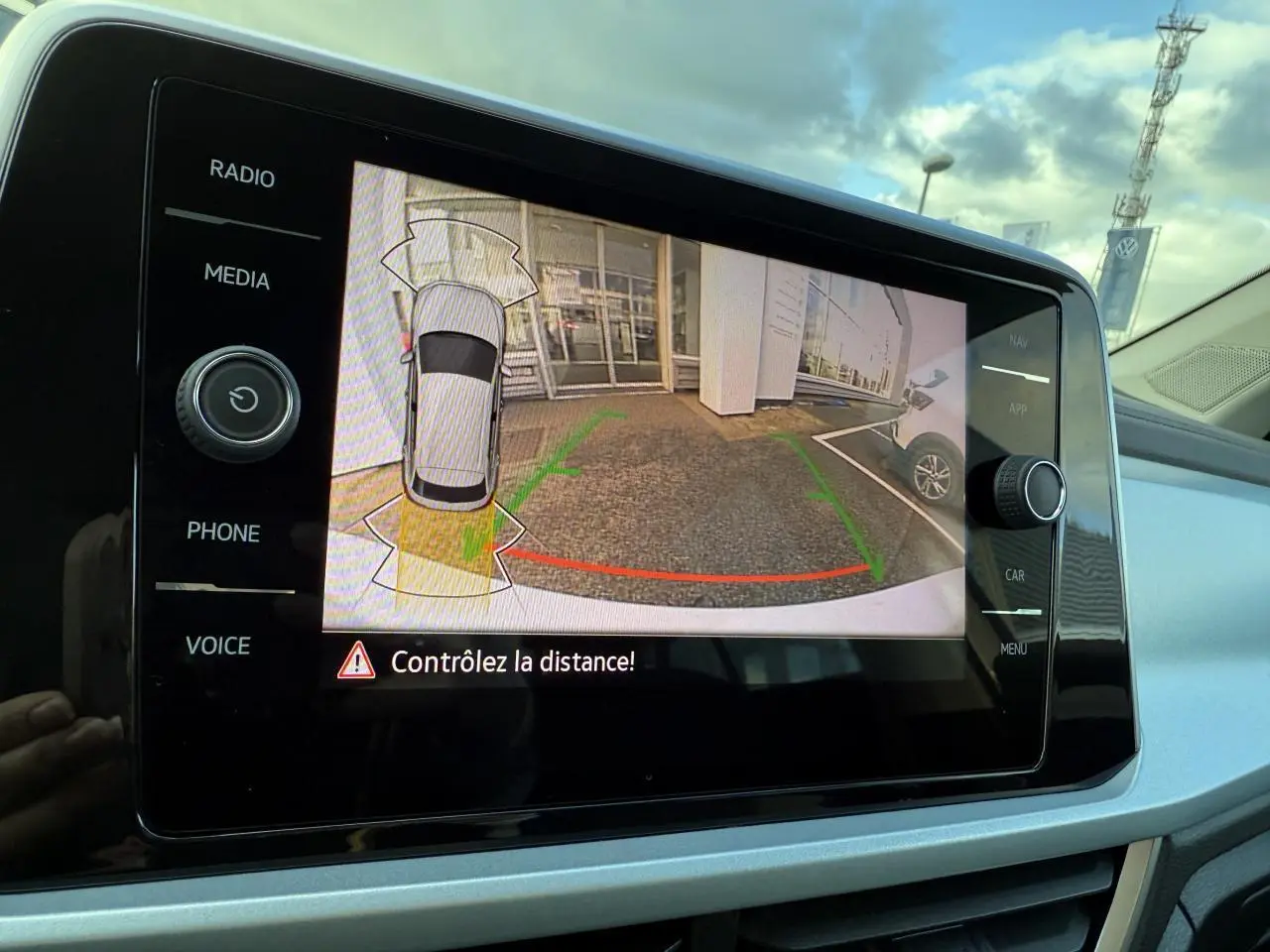 Écran tactile du système infotainment montrant la caméra de recul du Volkswagen T-Roc blanc pur en stationnement.