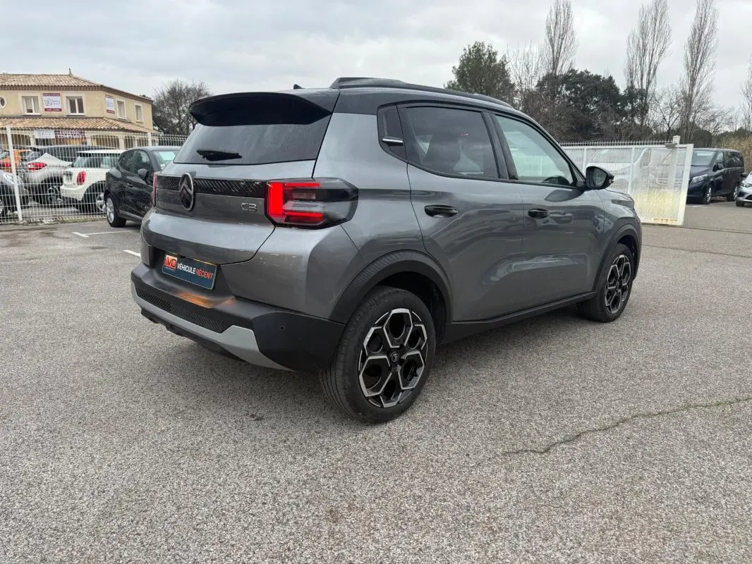 Vue 3/4 arrière droite d'une Citroën C3 gris métallisé avec jantes alliage noires et barres de toit visibles.