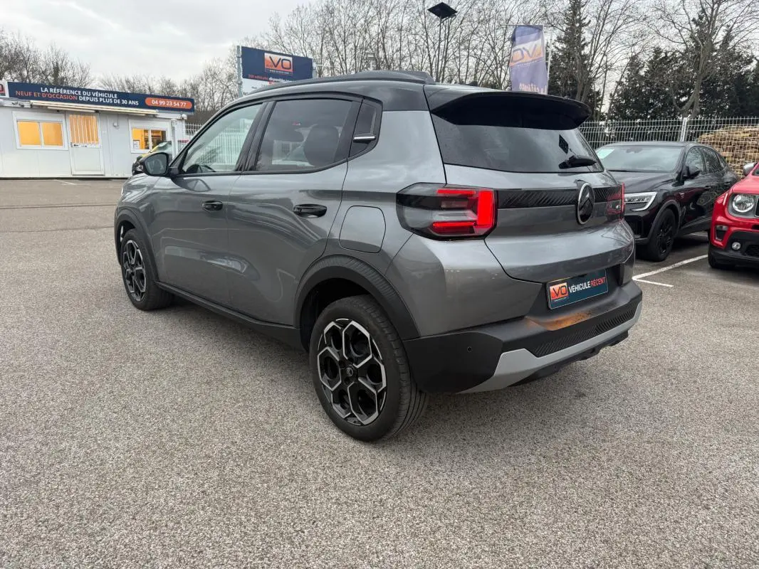 Vue 3/4 arrière droite d'une Citroën C3 gris métallisé avec jantes alliage 17 pouces et barres de toit noires.