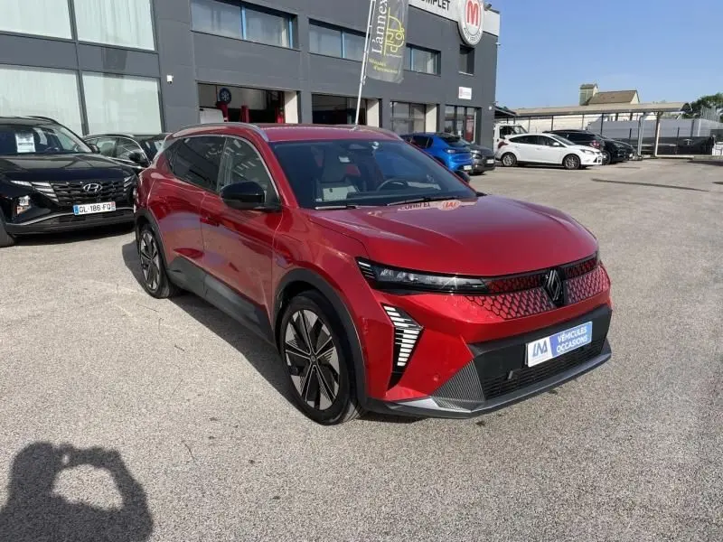 Renault Scenic E-Tech électrique rouge flamme, vue 3/4 avant droit, avec calandre lumineuse et jantes stylisées.