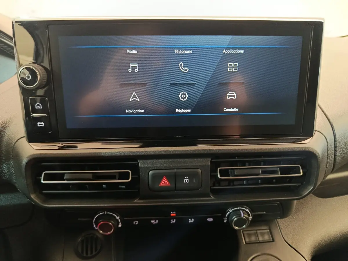 Écran tactile central du Peugeot Partner 2025 avec commandes climatisation et boutons de sécurité en vue frontale rapprochée.