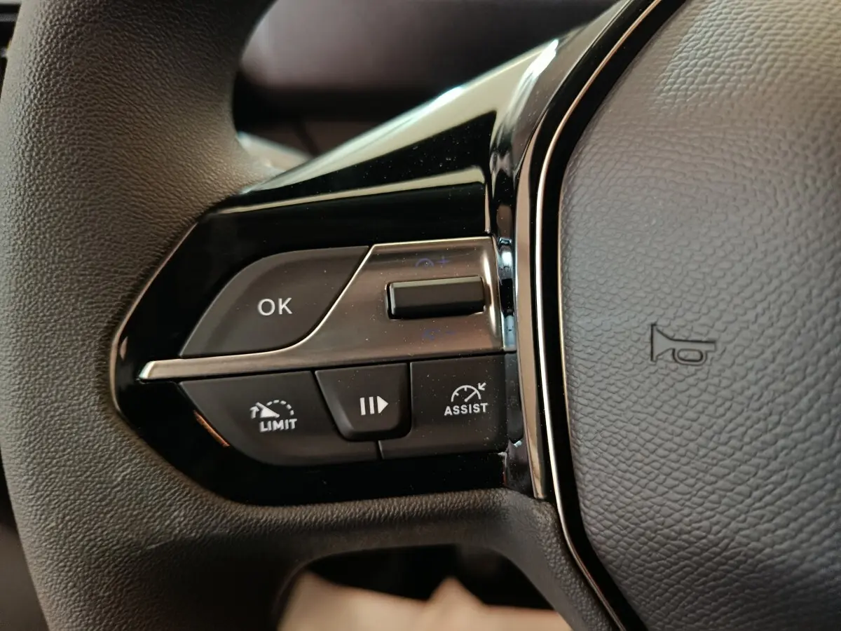 Gros plan sur les commandes à gauche du volant du Peugeot Partner blanc 2025, avec boutons de limitation et assistance.