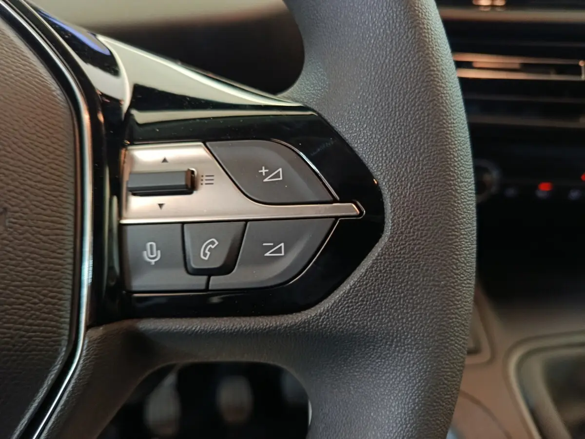 Gros plan sur les commandes multifonctions à gauche du volant du Peugeot Partner 2025, intérieur noir.