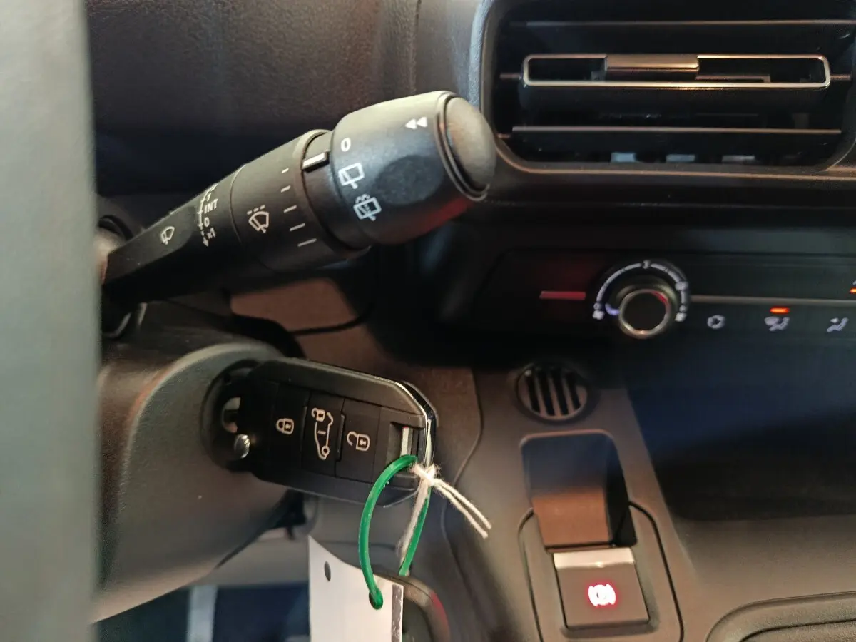 Gros plan intérieur sur la clé de contact insérée dans un Peugeot Partner blanc, avec commandes de climatisation et ventilation visibles.