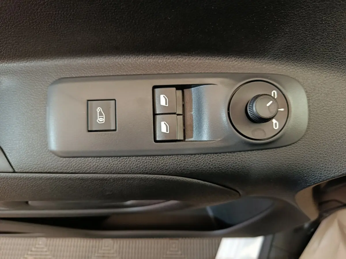 Vue rapprochée des commandes de réglage des rétroviseurs et des vitres sur la porte côté conducteur d’un Peugeot Partner blanc.