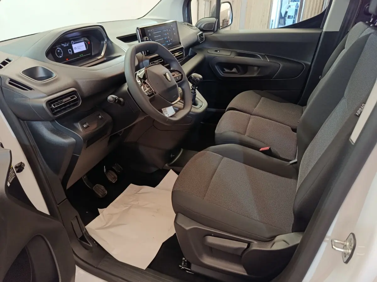 Intérieur avant droit du Peugeot Partner blanc 2025, montrant tableau de bord, volant et sièges tissu gris.