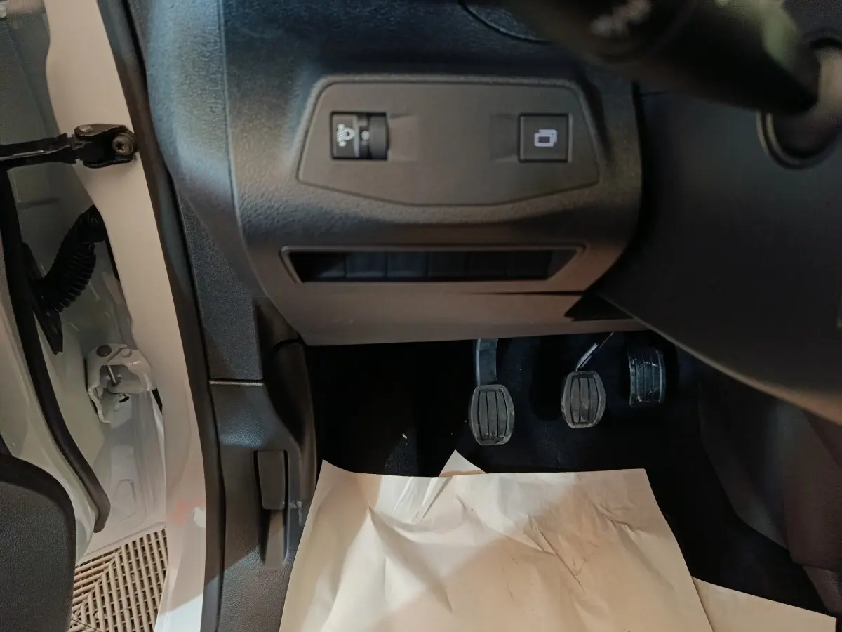 Vue intérieure côté conducteur du Peugeot Partner blanc 2025, montrant les pédales et commandes sous le tableau de bord.