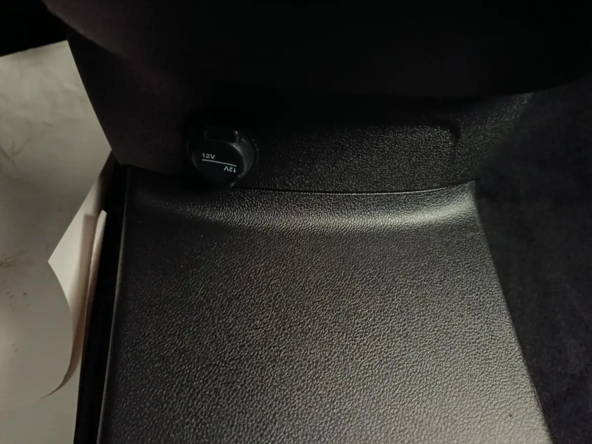 Prise 12V noire en gros plan sous le siège passager du Peugeot Partner blanc, vue intérieure rapprochée.