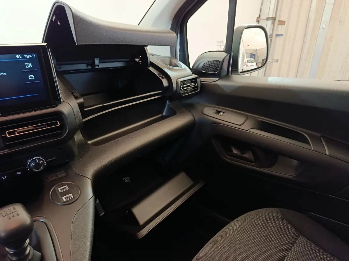 Intérieur du Peugeot Partner 2025 blanc, vue côté passager avec boîte à gants ouverte et tableau de bord moderne.