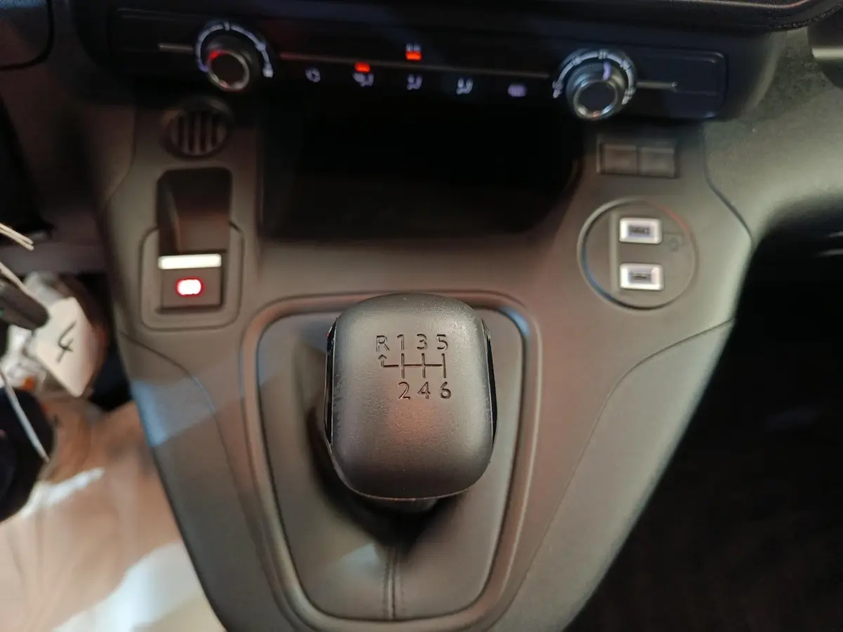 Gros plan sur le levier de vitesses manuel noir du Peugeot Partner blanc 2025, avec commandes et ports USB visibles.