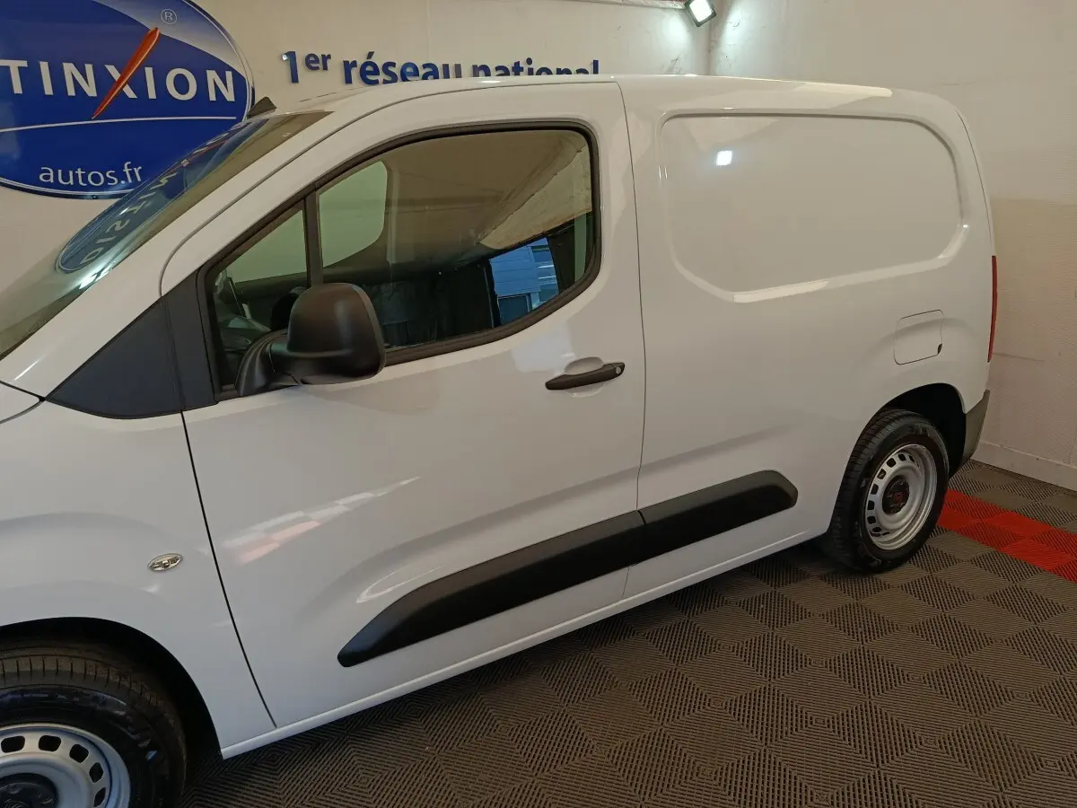 Vue de profil côté gauche du Peugeot Partner blanc, mettant en valeur la porte latérale pleine et les protections noires.
