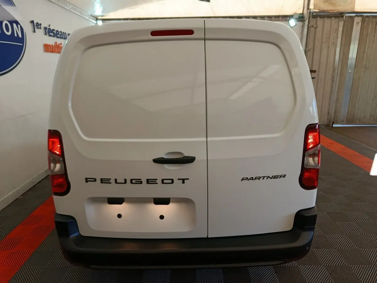 Vue arrière d'un utilitaire blanc Peugeot Partner avec portes battantes et feux arrière allumés en intérieur.