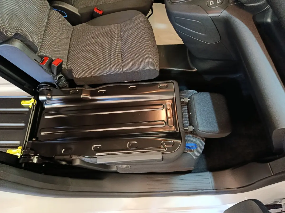Vue intérieure plongeante sur le siège passager relevé du Peugeot Partner blanc, montrant la structure métallique et l'assise grise.