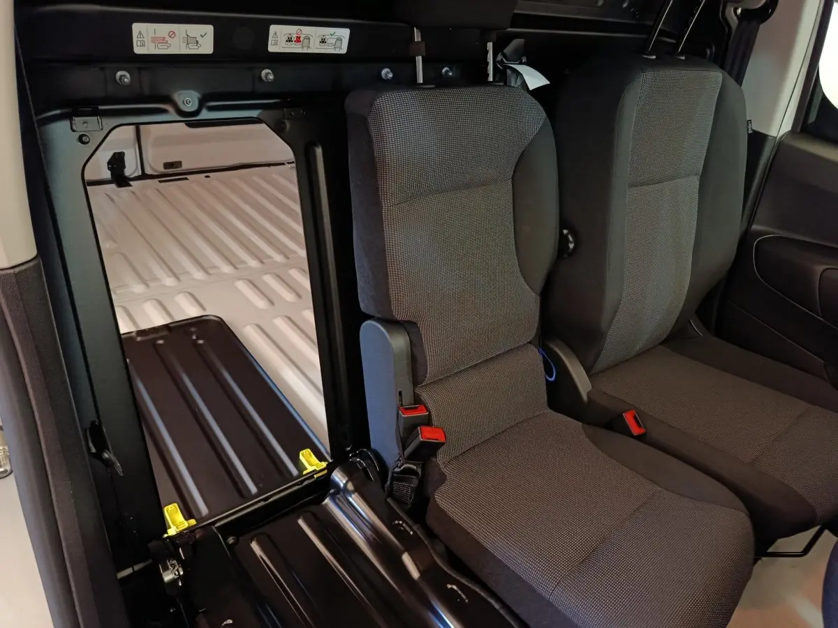 Vue intérieure du Peugeot Partner blanc 2025 montrant les sièges avant et l’espace de chargement derrière la cloison pleine.