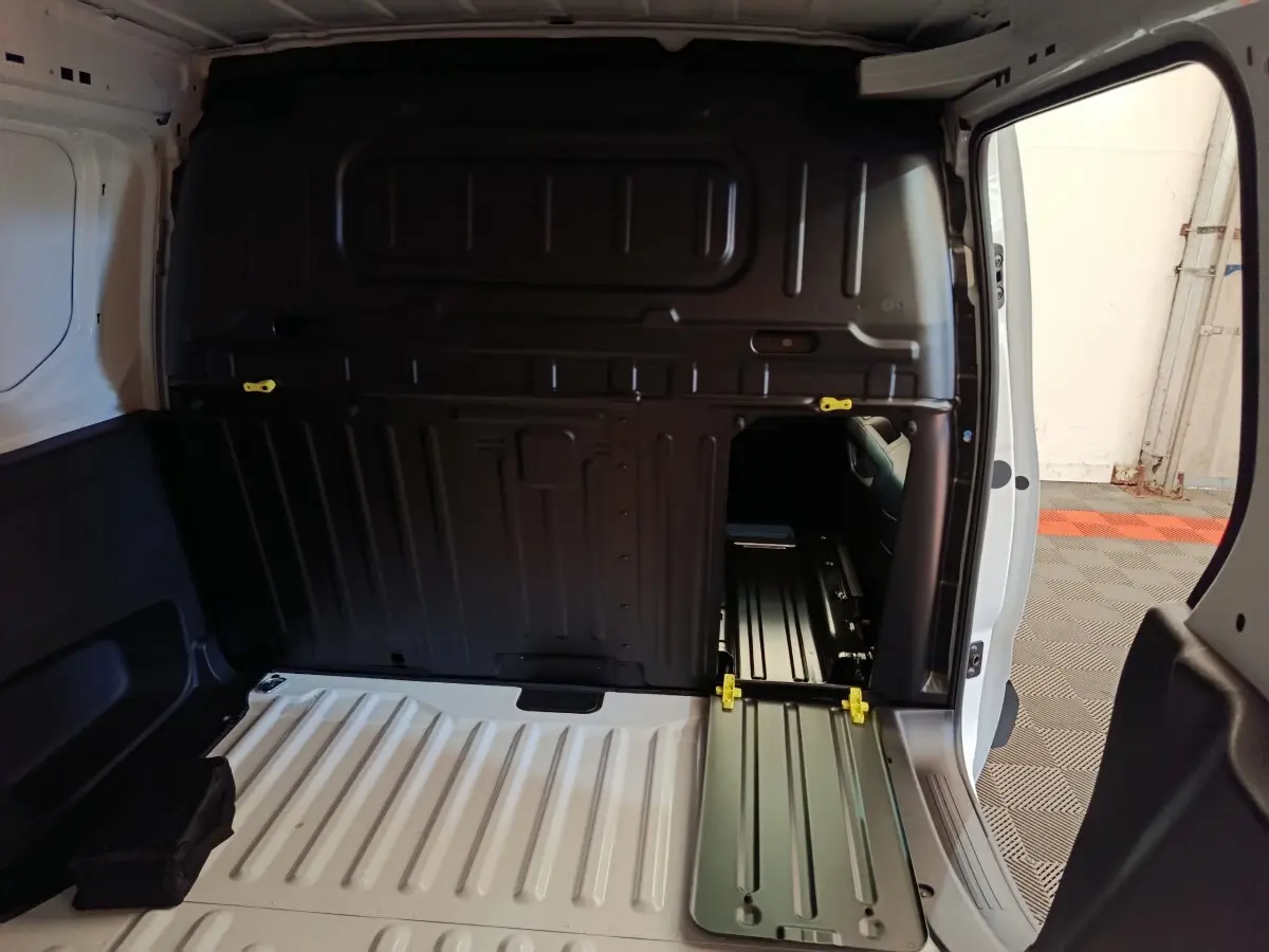 Vue intérieure arrière du Peugeot Partner blanc 2025 montrant la cloison pleine avec trappe de passage et plancher métallique.