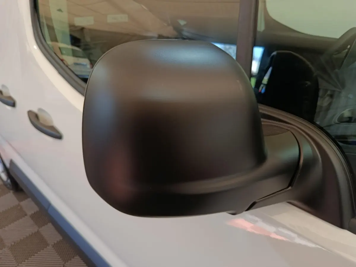 Rétroviseur noir en gros plan sur le côté gauche d’un Peugeot Partner blanc, vue latérale partielle.