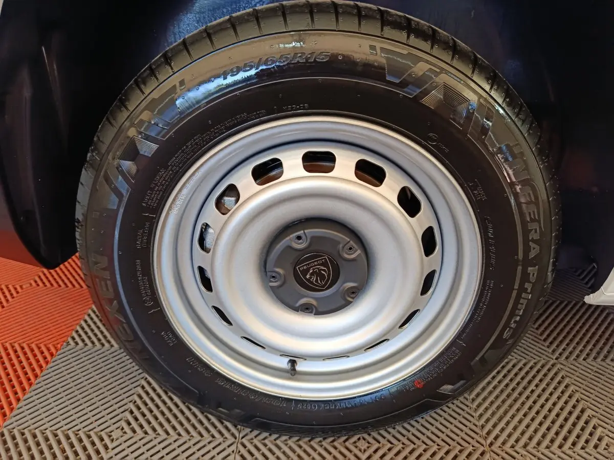 Gros plan sur la roue acier grise avec logo Peugeot, montée sur un Peugeot Partner blanc, vue latérale.