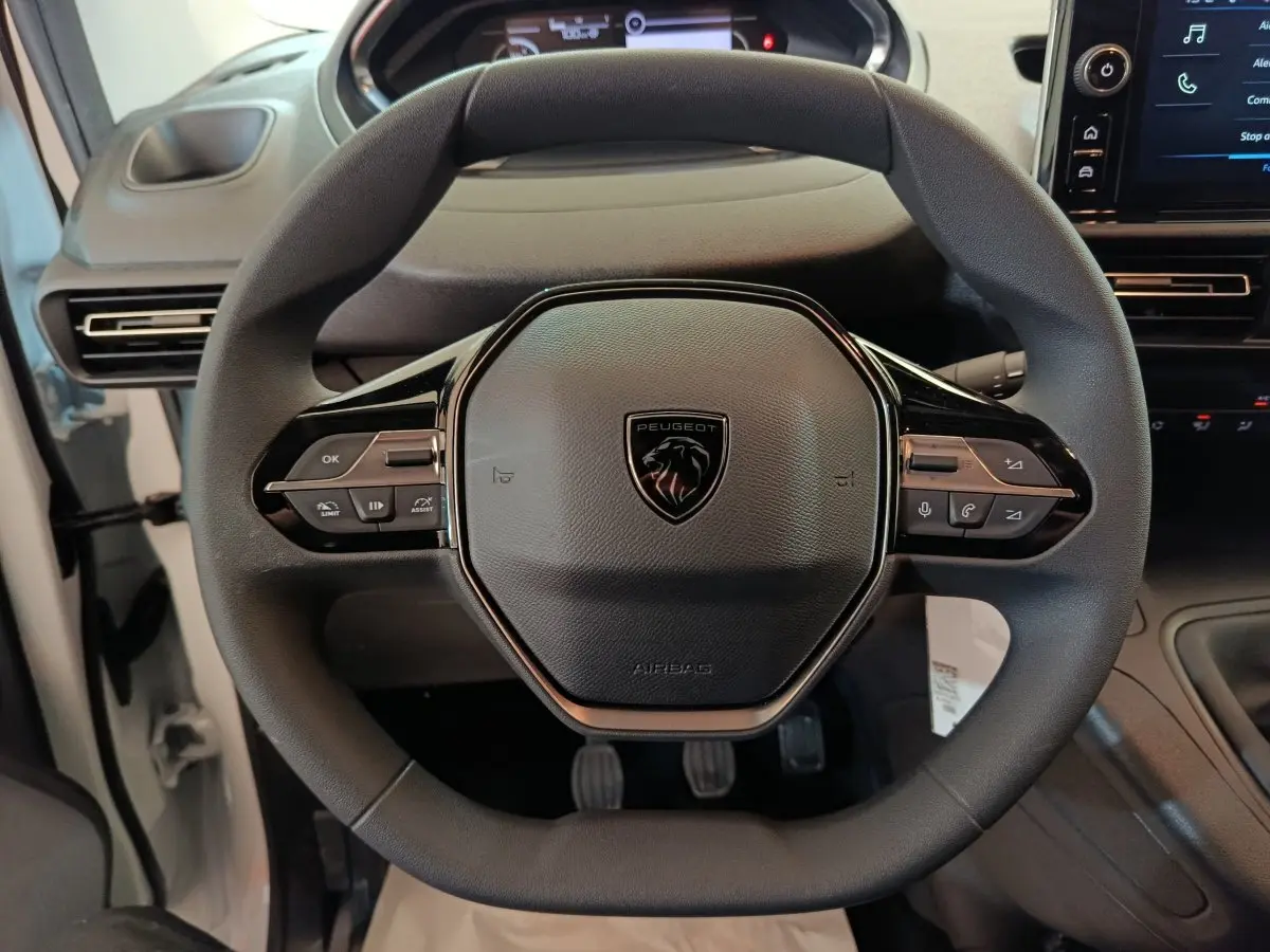 Vue rapprochée du volant noir du Peugeot Partner 2025, avec commandes intégrées et tableau de bord partiellement visible.