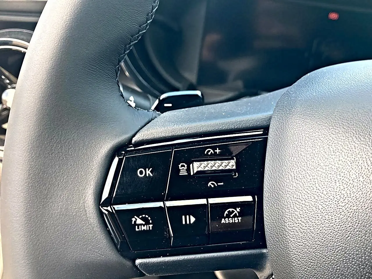 Gros plan sur les commandes noires au volant gris de l'Alfa Romeo Junior 1.2 hybride 2026, boutons de régulateur et assistance.