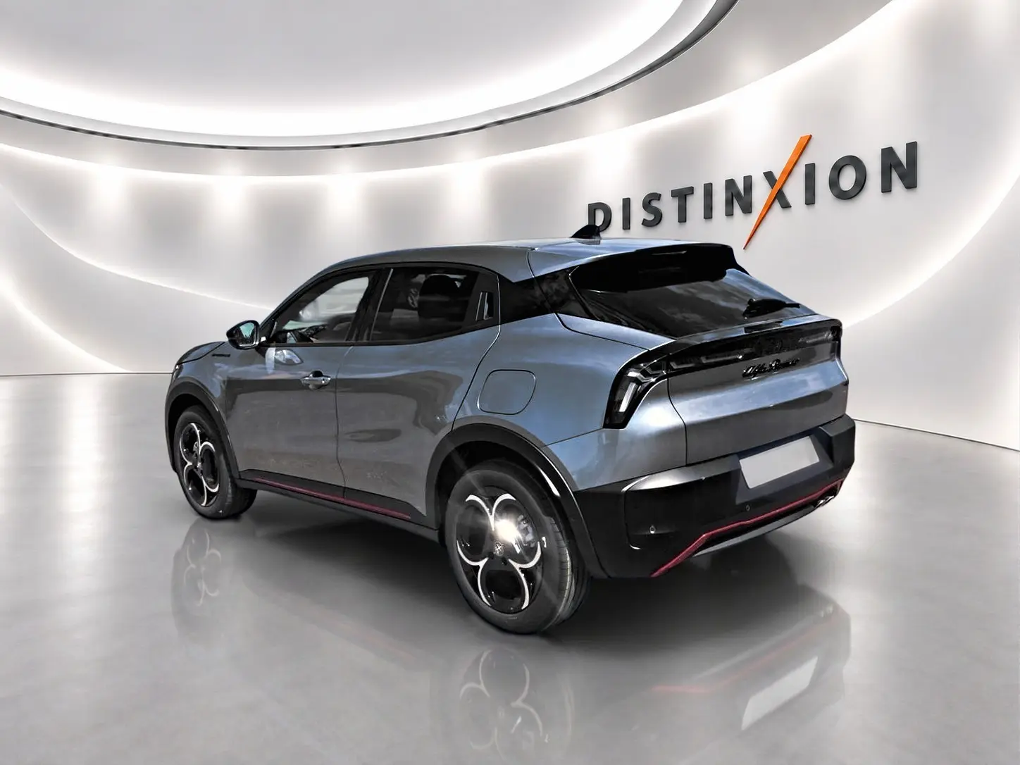 Vue 3/4 arrière droite d'une Alfa Romeo Junior gris métallisé avec jantes alliage et toit noir dans un showroom lumineux.
