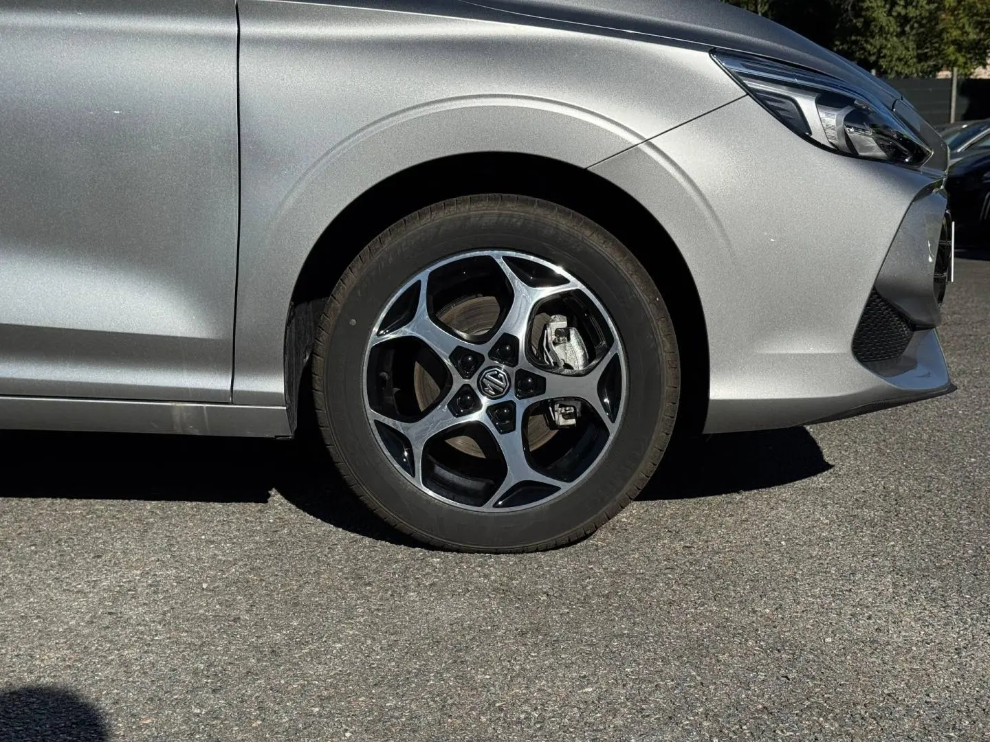 Gros plan sur la roue avant gauche et partie avant d'une MG3 Cosmic Silver métallisé avec jante alu noire et argent.