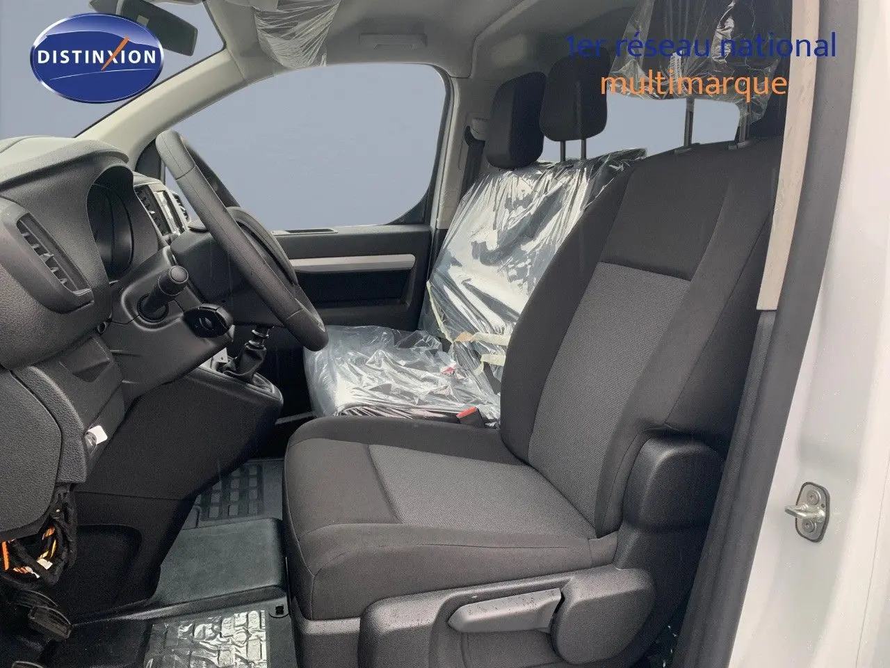 Vue intérieure côté conducteur du Peugeot Expert cabine approfondie blanc, sièges noirs avec protections plastiques visibles.