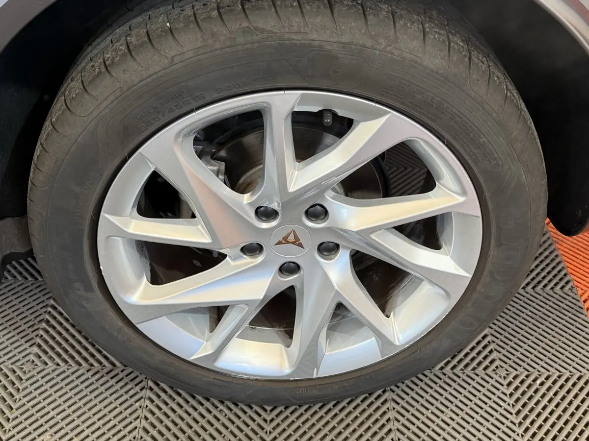 Gros plan sur la jante argentée au design dynamique avec logo CUPRA, roue montée sur un véhicule noir.