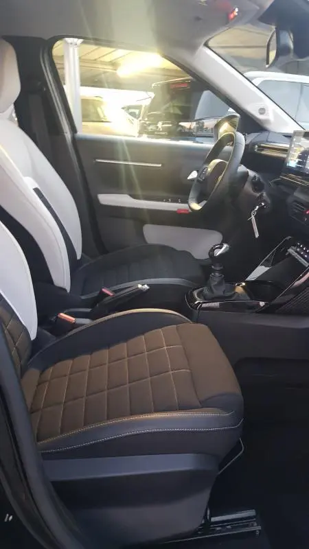 Vue intérieure côté conducteur de la Citroën C3 Turbo 100 ch 2025 noire, sièges bi-ton et boîte manuelle visible.