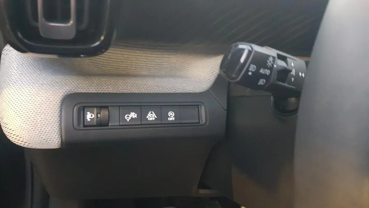 Gros plan sur les commandes d'assistance et réglage des phares à gauche du volant dans une Citroën C3 noire 2025.