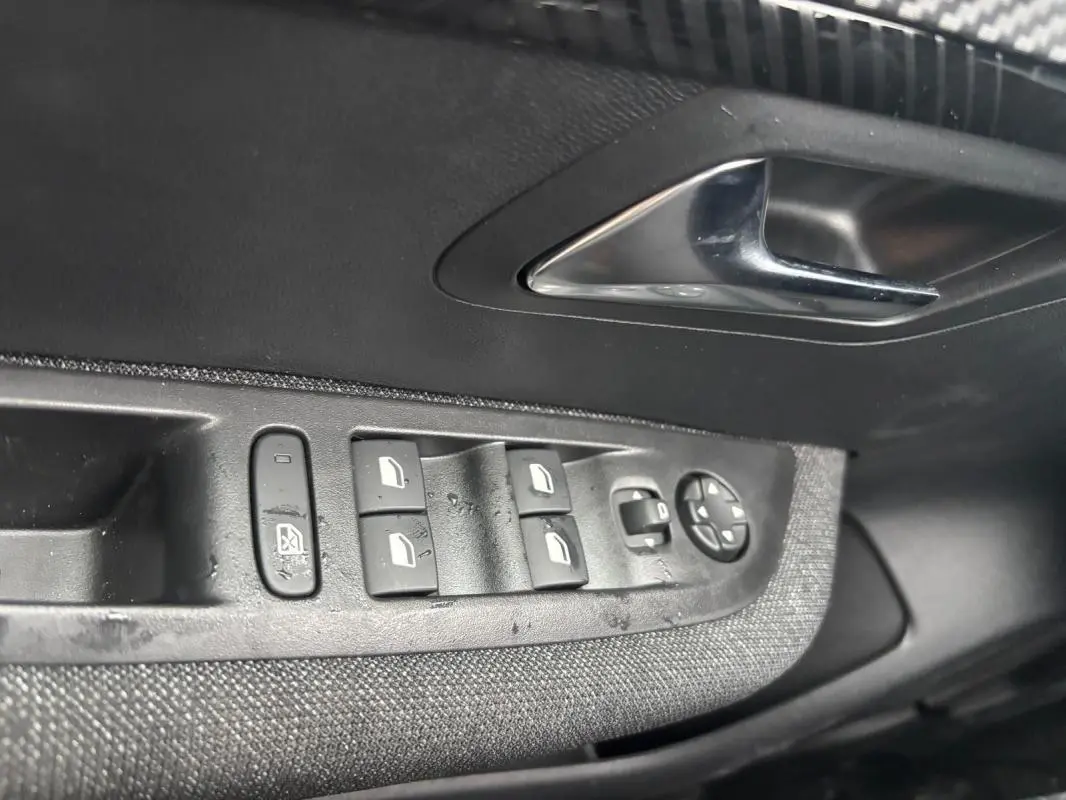 Gros plan sur la commande des vitres électriques côté conducteur d’une Peugeot 208 Hybrid gris, avec poignée de porte chromée.