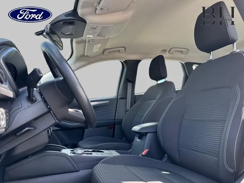 Vue intérieure côté conducteur du Ford Kuga 2023, sièges sport noirs avec surpiqûres blanches et volant cuir multifonction.