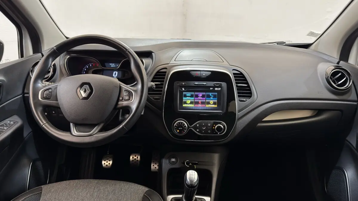 Vue intérieure avant du tableau de bord noir du Renault Captur Intens TCe 90 avec volant cuir multifonctions et écran tactile central.