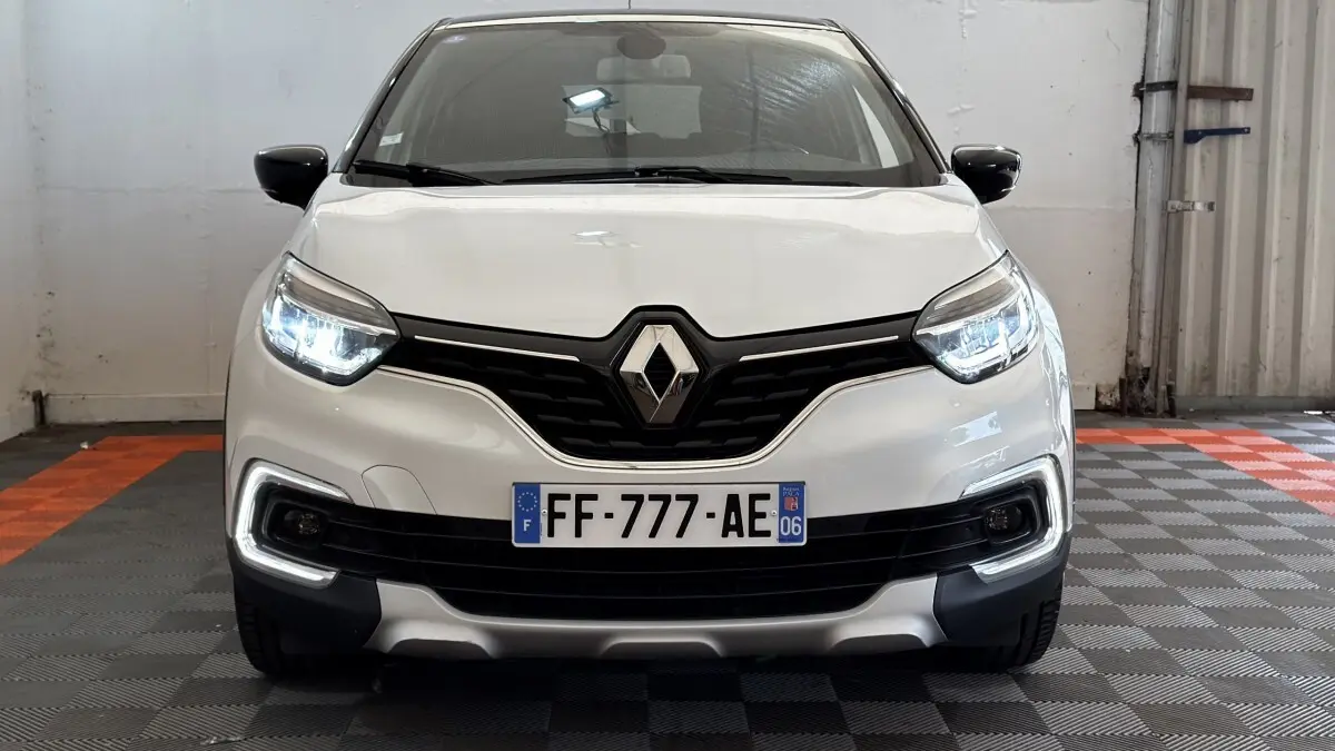 Vue avant d'un Renault Captur Intens TCe 90 blanc avec phares LED allumés et calandre noire distinctive.