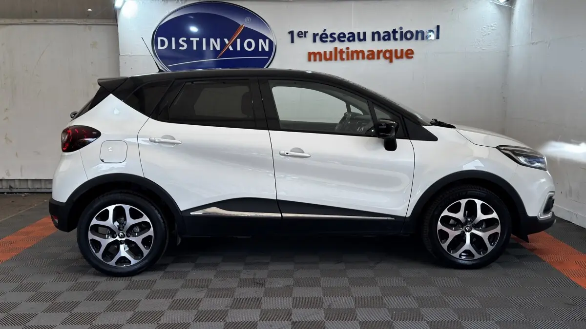 Profil droit du Renault Captur blanc 2019 avec toit noir et jantes alliage bicolores, stationné en intérieur.